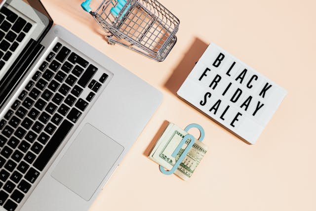 Imagem com um laptop, dinheiro na mesa e uma placa da black friday